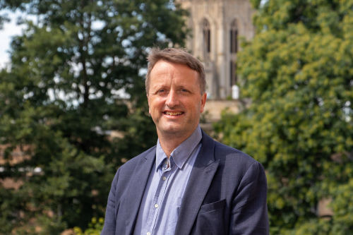 Professor Steve Eichhorn in a suit in front of trees and university building